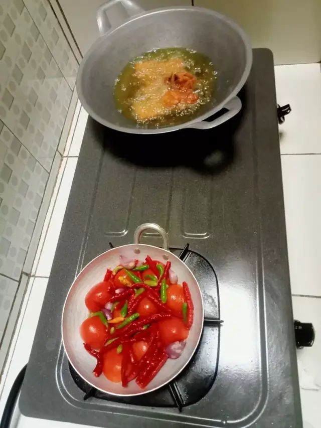 Cobek berisi cabe merah dan tomat di sebelah wajan penggorengan