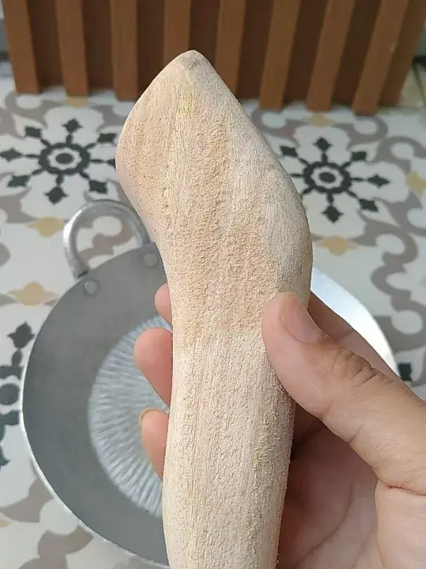 Ulekan kayu digenggam dari dekat, cobek tampak samar di belakang